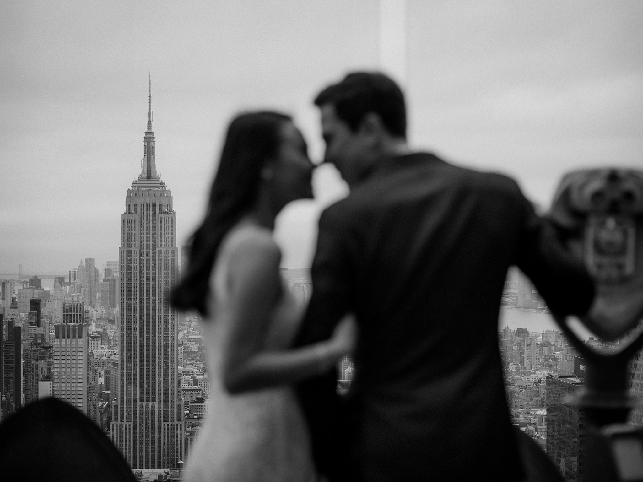Engaged couple looking into each others eyes on rooftop with view of Empire State Building
