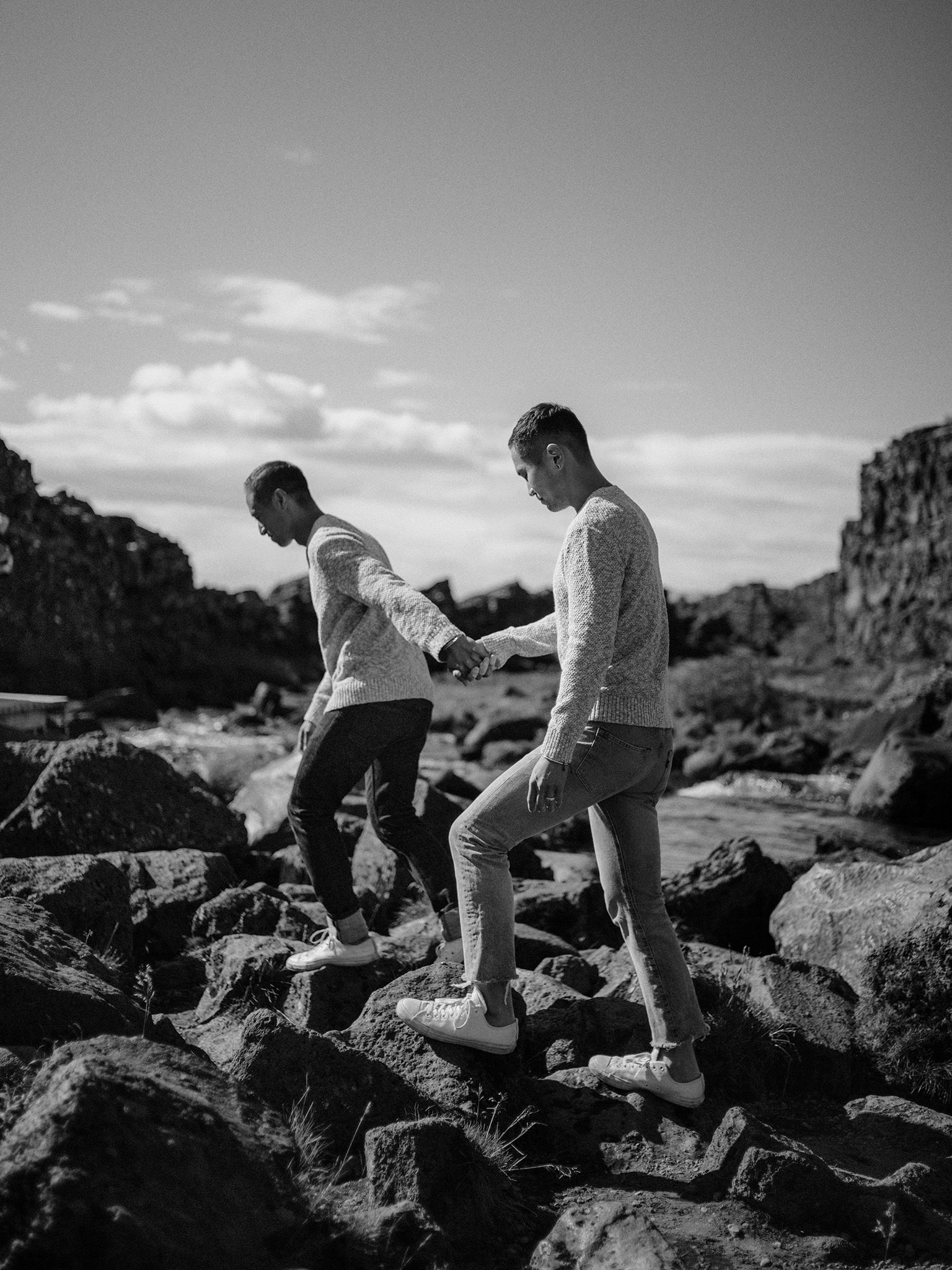 Same sex male couple holding hands as they walk over rocks in gorge