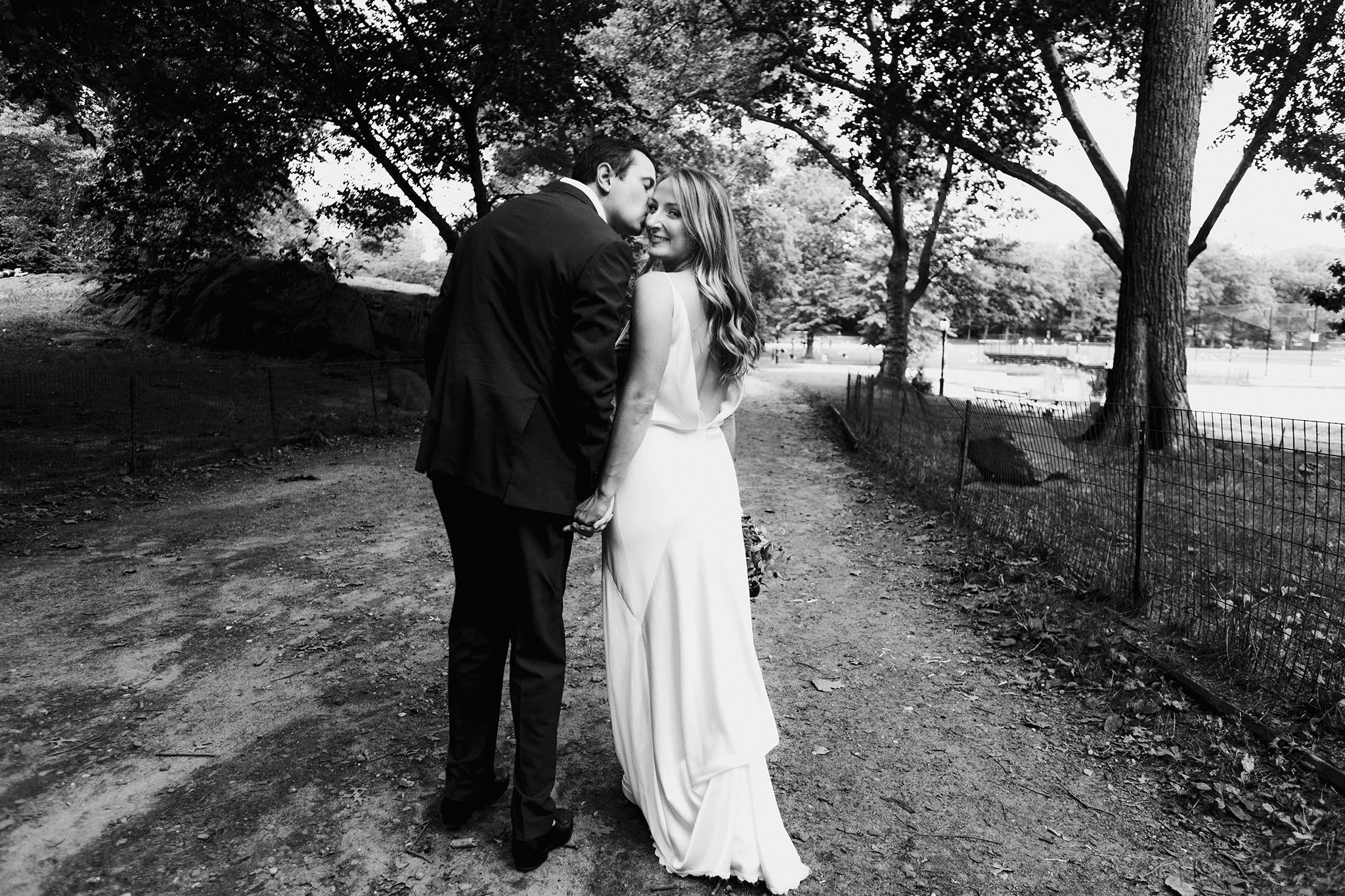 Groom kisses his bride on the cheek while they walk through Central Park, Manhattan