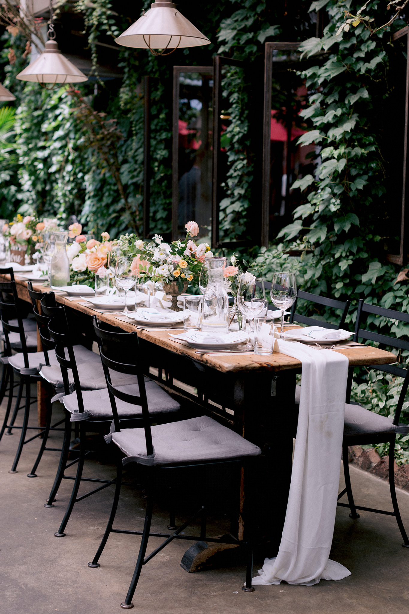Ivy covered patio with a long dining table set with blush roses. 