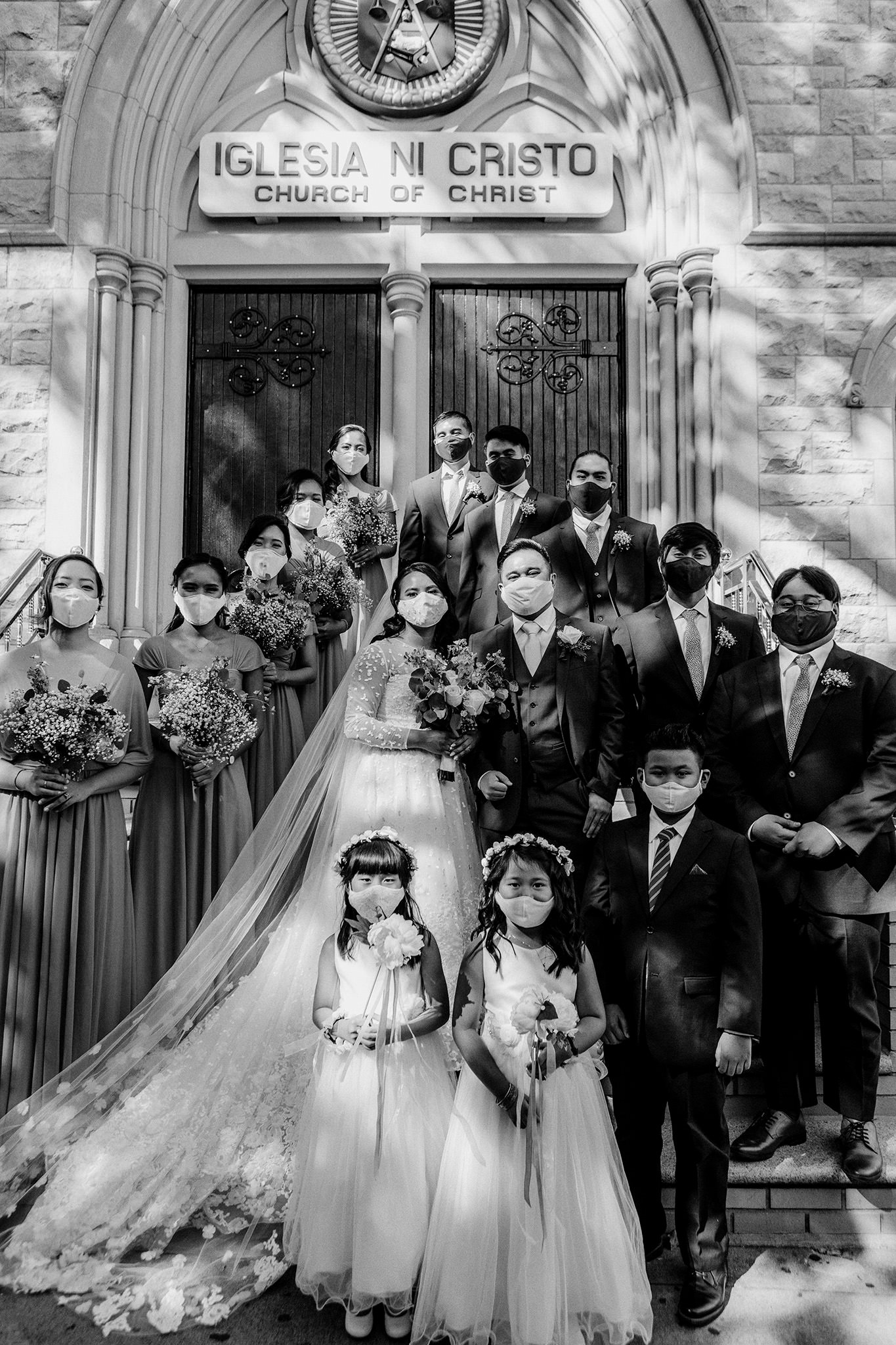 Entire wedding party in front of church steps with masks on during COVID19 pandemic.