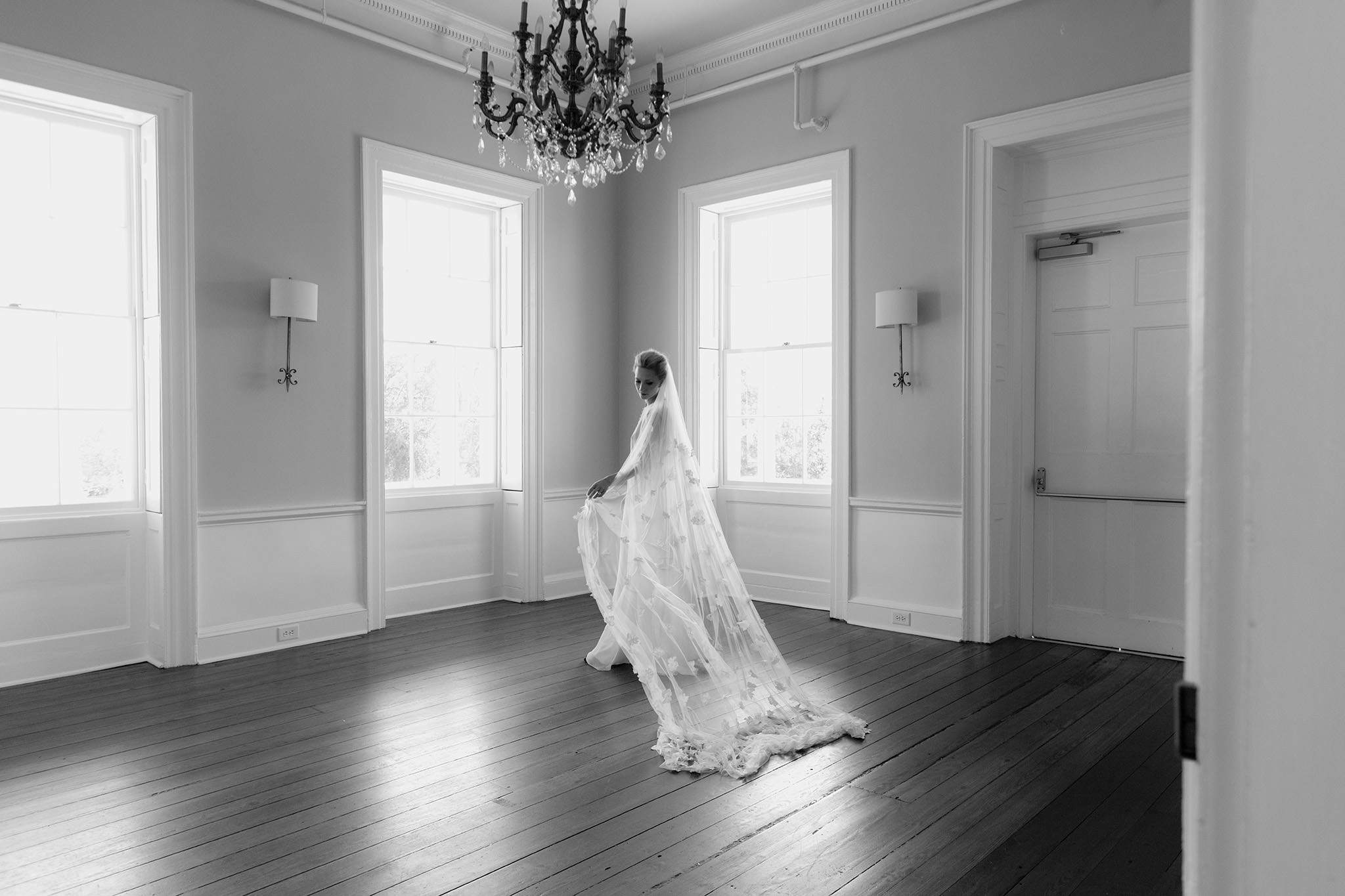Woman fanning out long bridal veil in empty room with chandelier