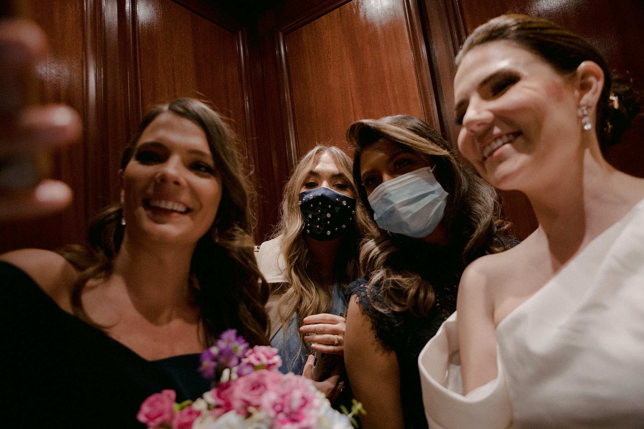 Bride and bridesmaids smiling for a selfie with masks on