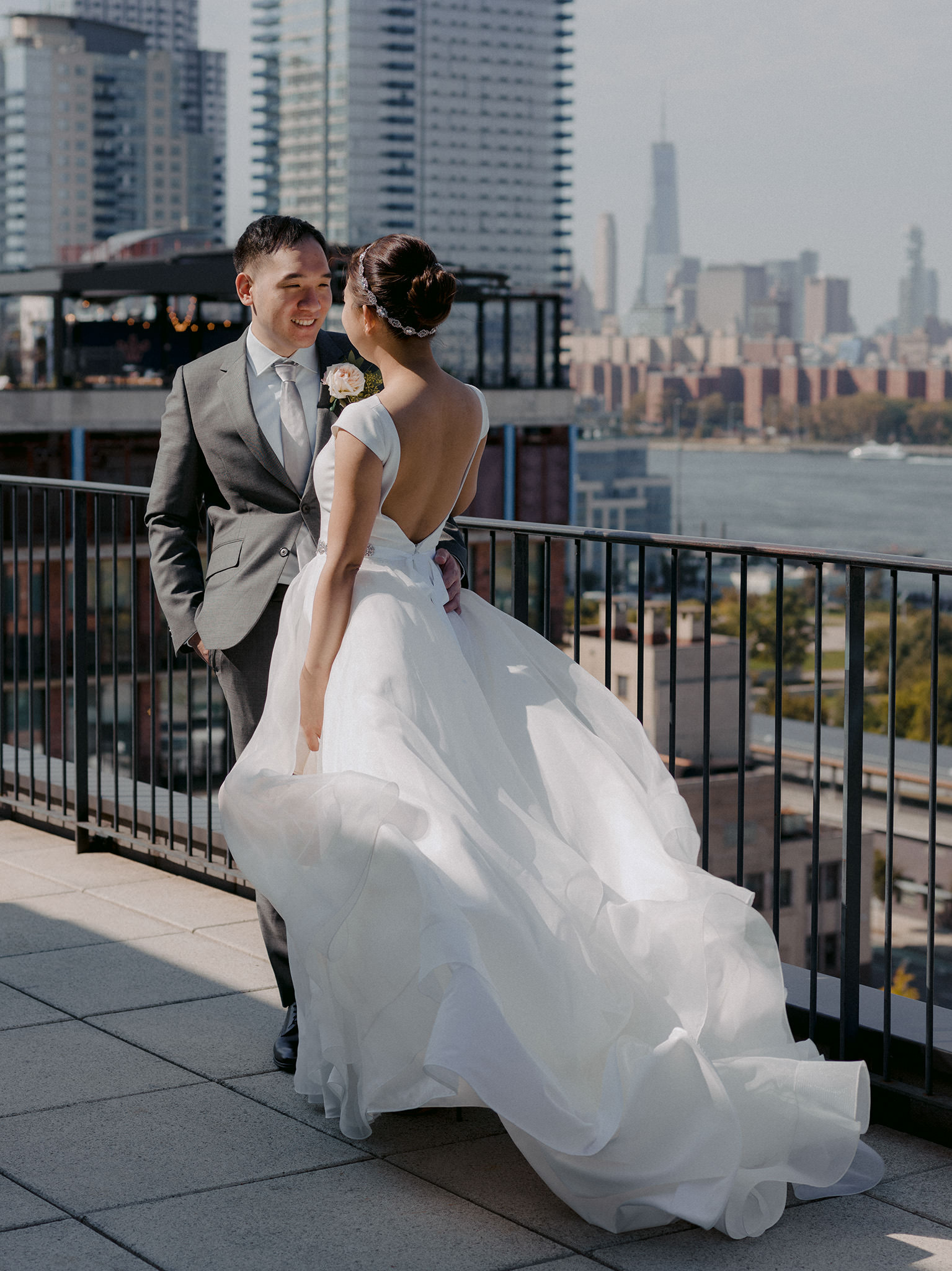 groom looking at his bride on their wedding day at the Wythe Hotel rooftop with One World Trade in the background; bride's dress is flowing in the wind