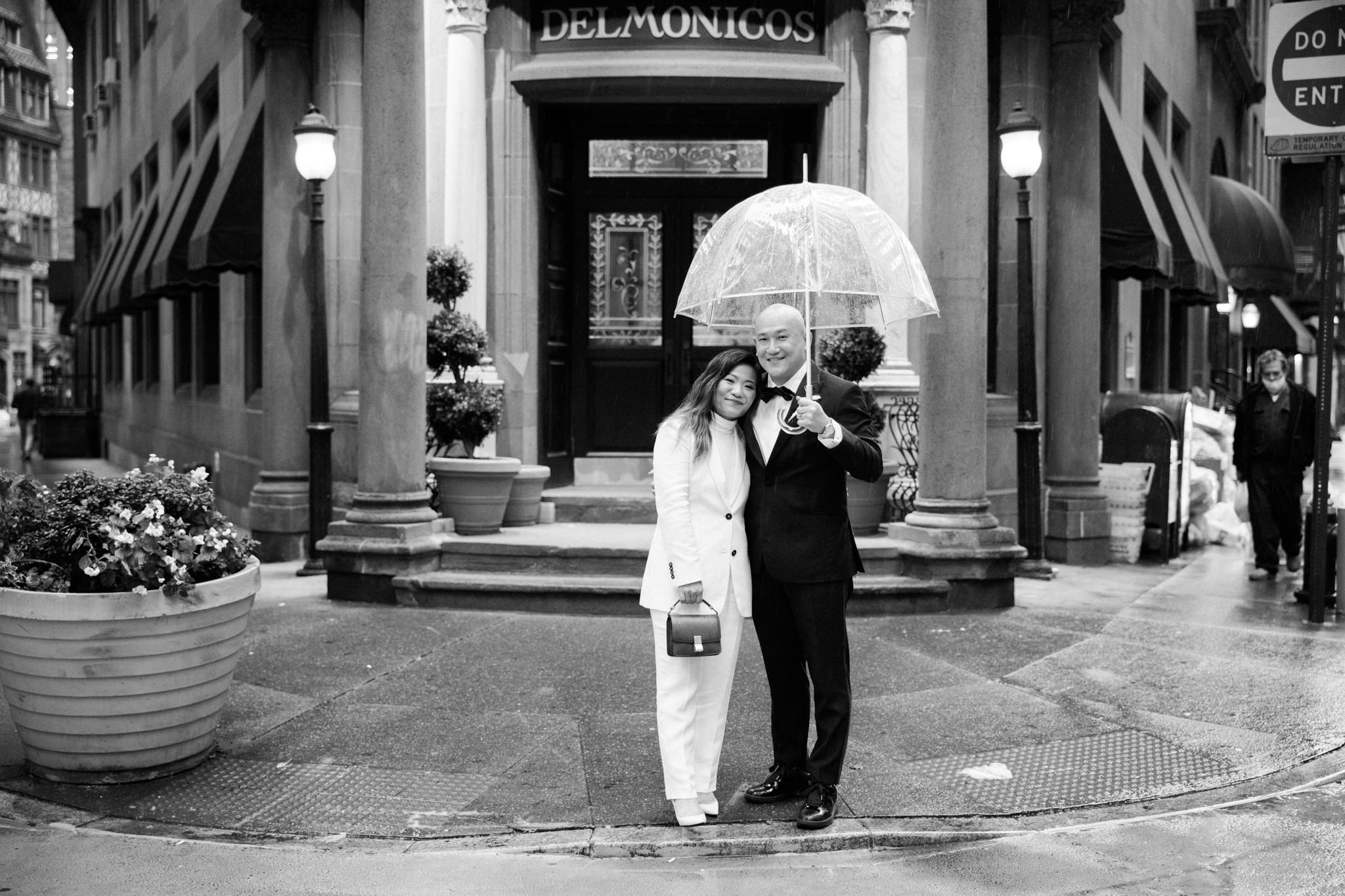 Groom holds an umbrella for his bride outside of Delmonicos in New York City