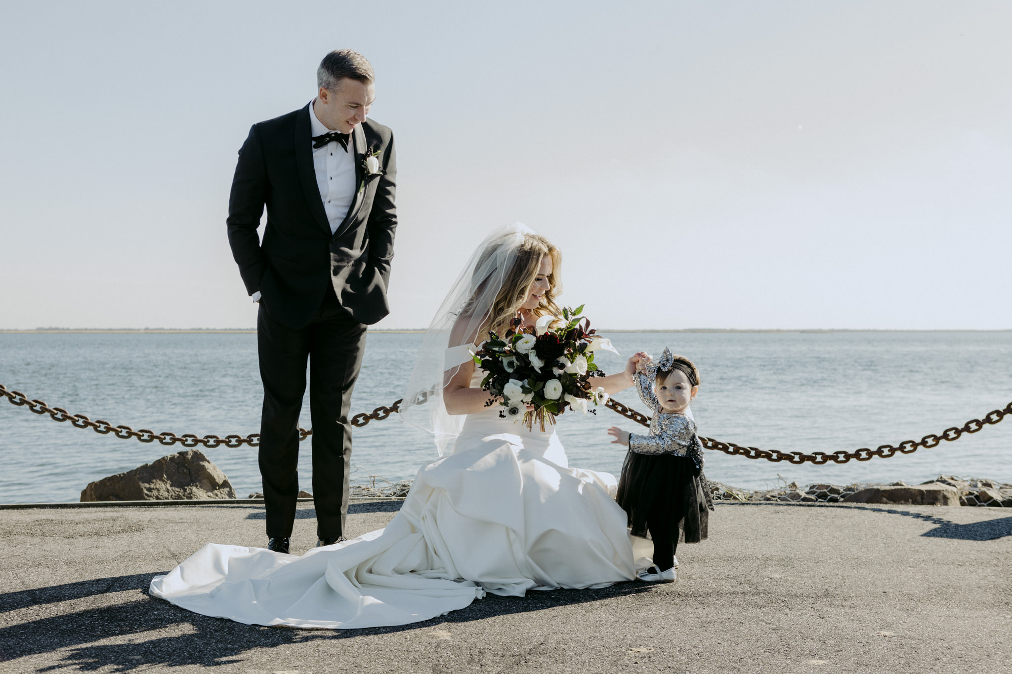 Bride crouches down to hold her flower girls hand