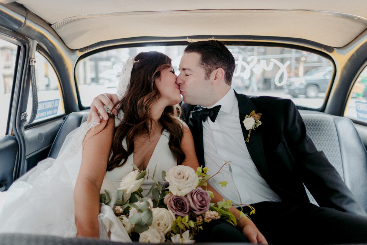 Bride and groom kiss in the back of a vintage nyc taxi on their wedding day