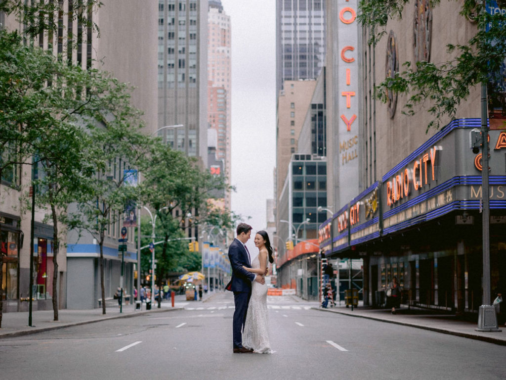 A bride is held by her groom in the street outside of Radio City Music Hall for their wedding photos