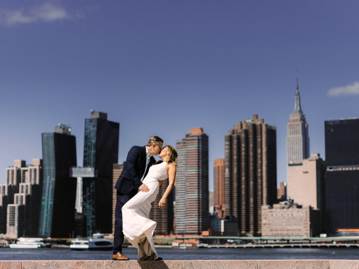 A groom dips his bride in a kiss with the New York City skyline in the background