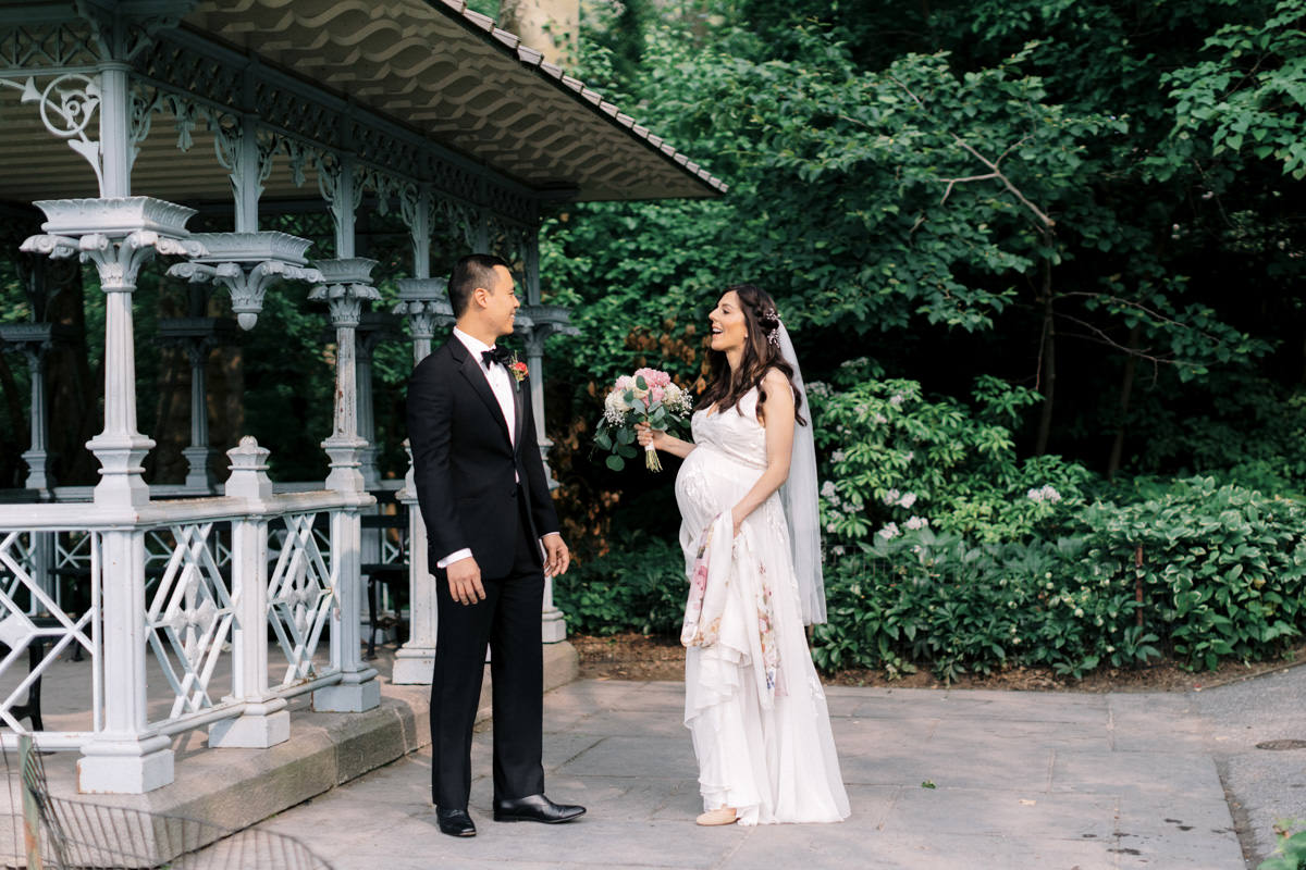 A pregnant bride and her groom take wedding photos at the Ladies Pavilion in NYC