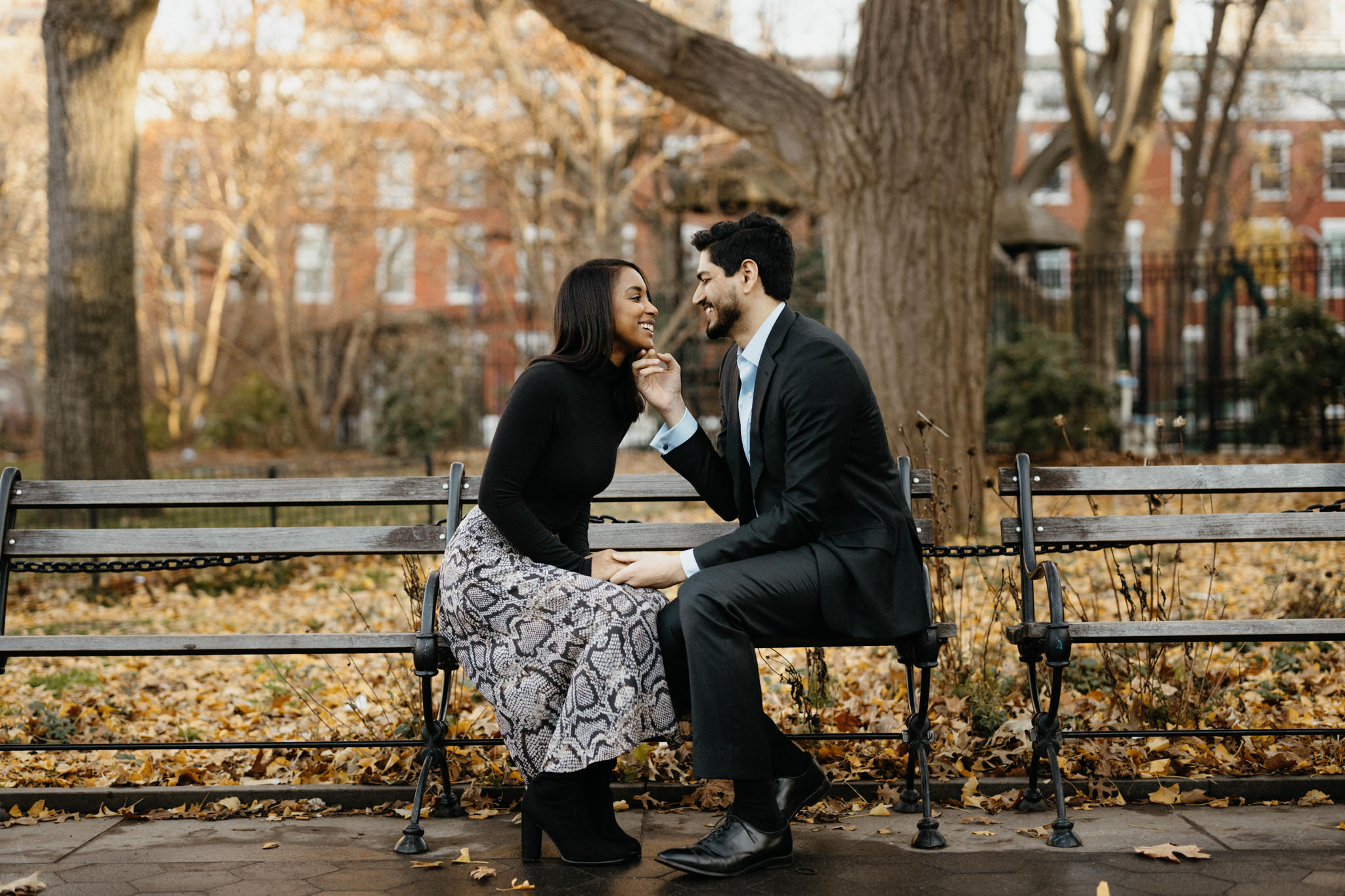 A bi racial couple sits on a bench in Washington Square Park talking about their proposal