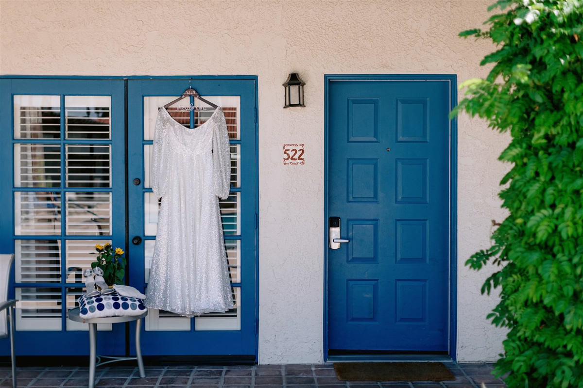 Wedding photographer takes a photo of a wedding dress hanging in a blue window