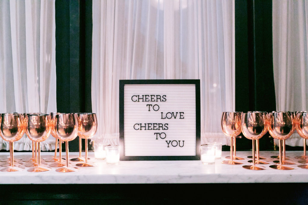 A sign with rose gold wine glasses on a table