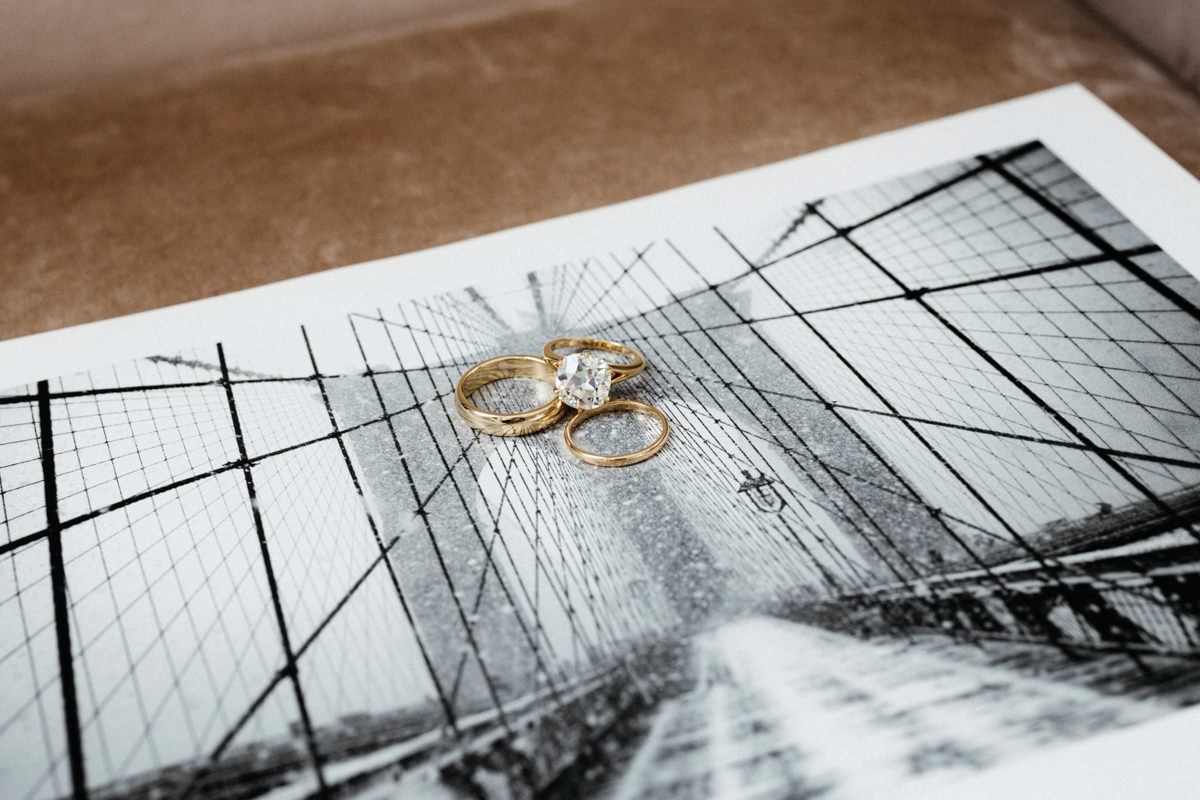 The diamond engagement ring and wedding bands are placed on top of a brooklyn bridge photograph. Image by Jenny Fu Studio