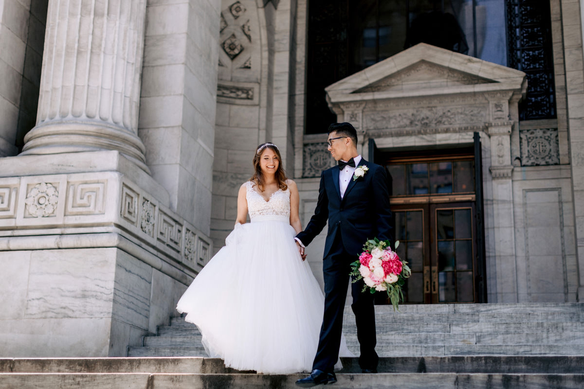 A bride and groom walk down the steps of their wedding venue, the NYPL, New York public library