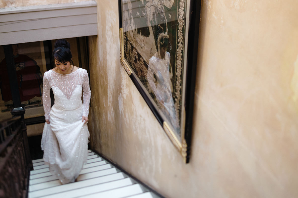 Bride in a beaded wedding dress walks up a staircase at her wedding venue