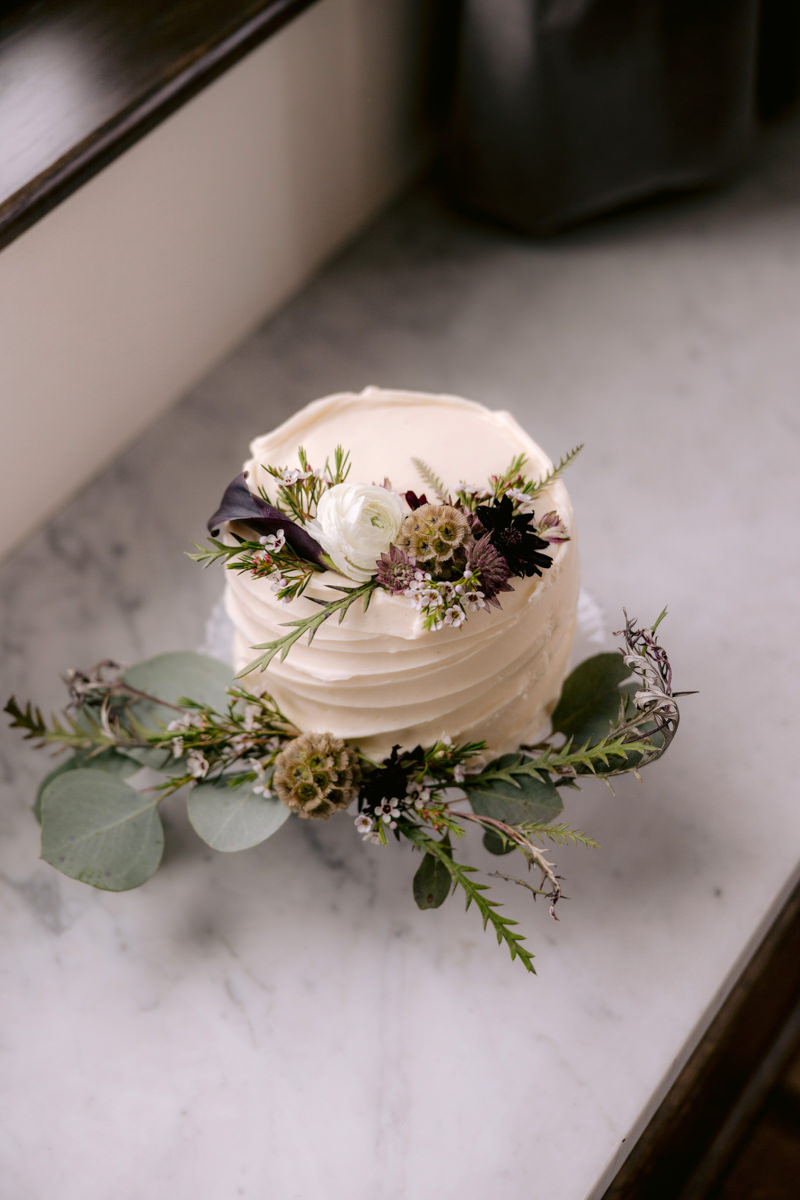 A wedding cake sits on a counter with foliage as decoration
