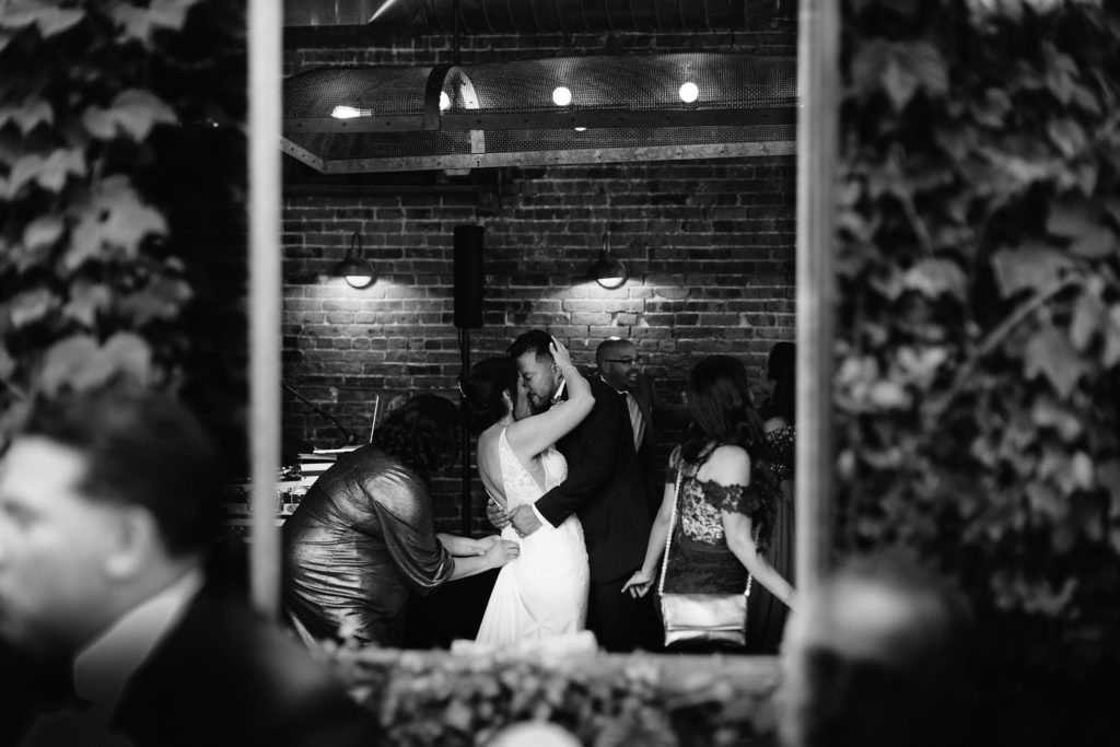 A wedding photographer takes a picture of the bride and groom through a mirror