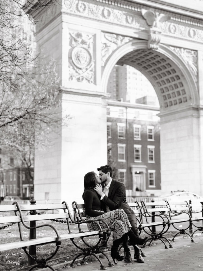 A man and woman kiss on a park bench during an engagement photoshoot