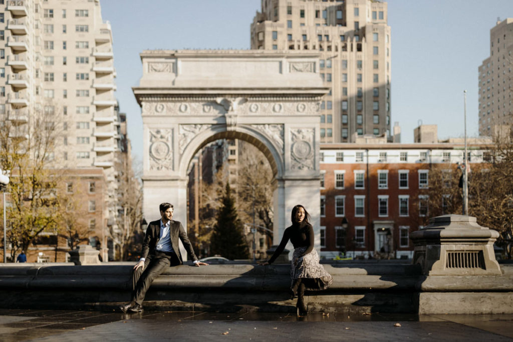 A man and women sit in a park for their engagement photos