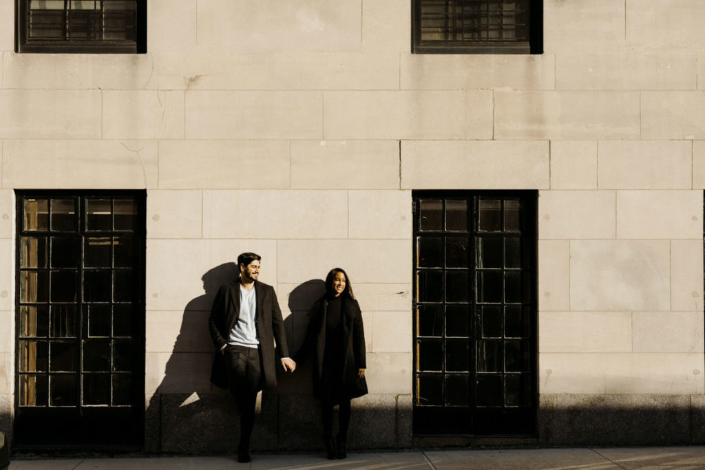 Man and woman lean against a wall holding hands