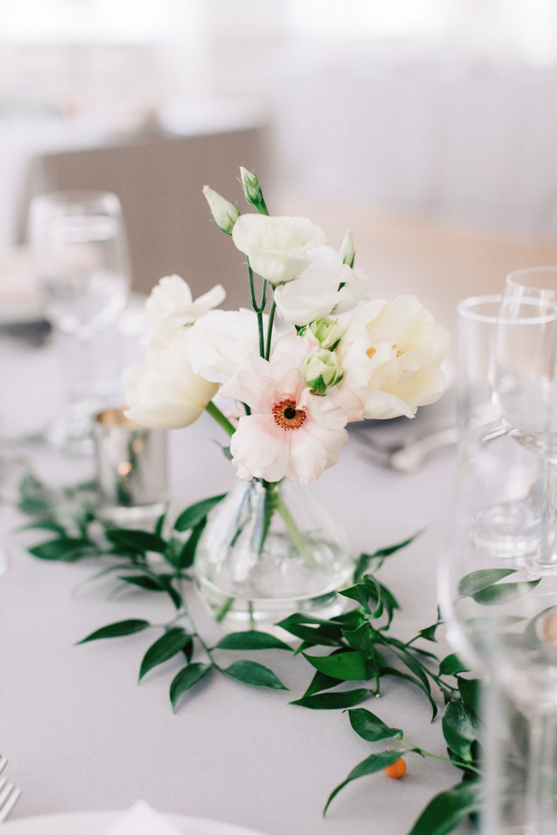 Garden roses and carnations in a bud vase on a table at a wedding reception