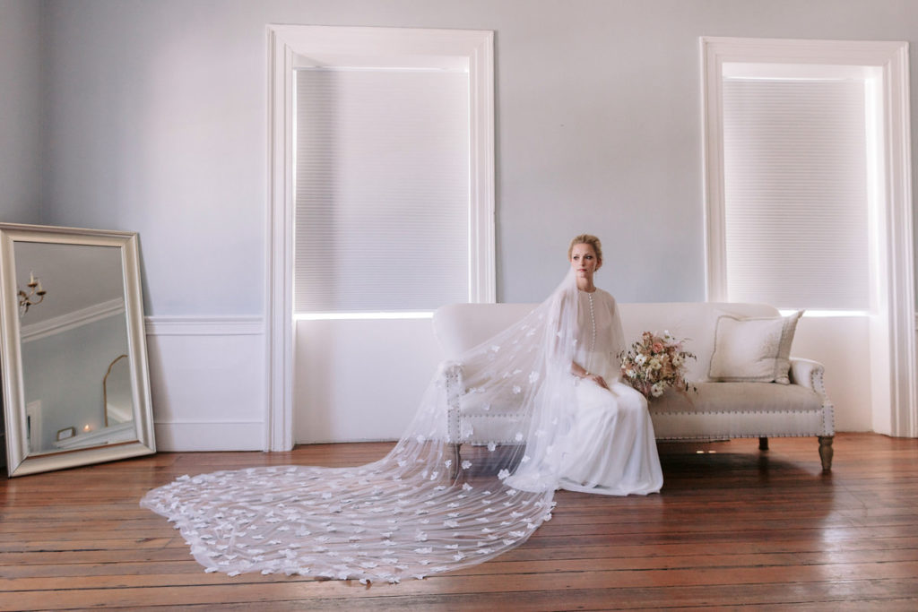 A bride sits on a couch with her veil fanned out onto the floor