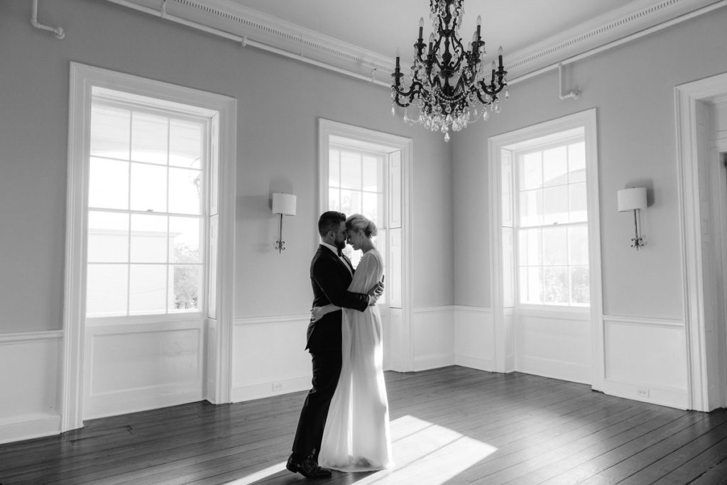 Man and woman hold each other in an embrace in a room with tall ceilings and wood floors
