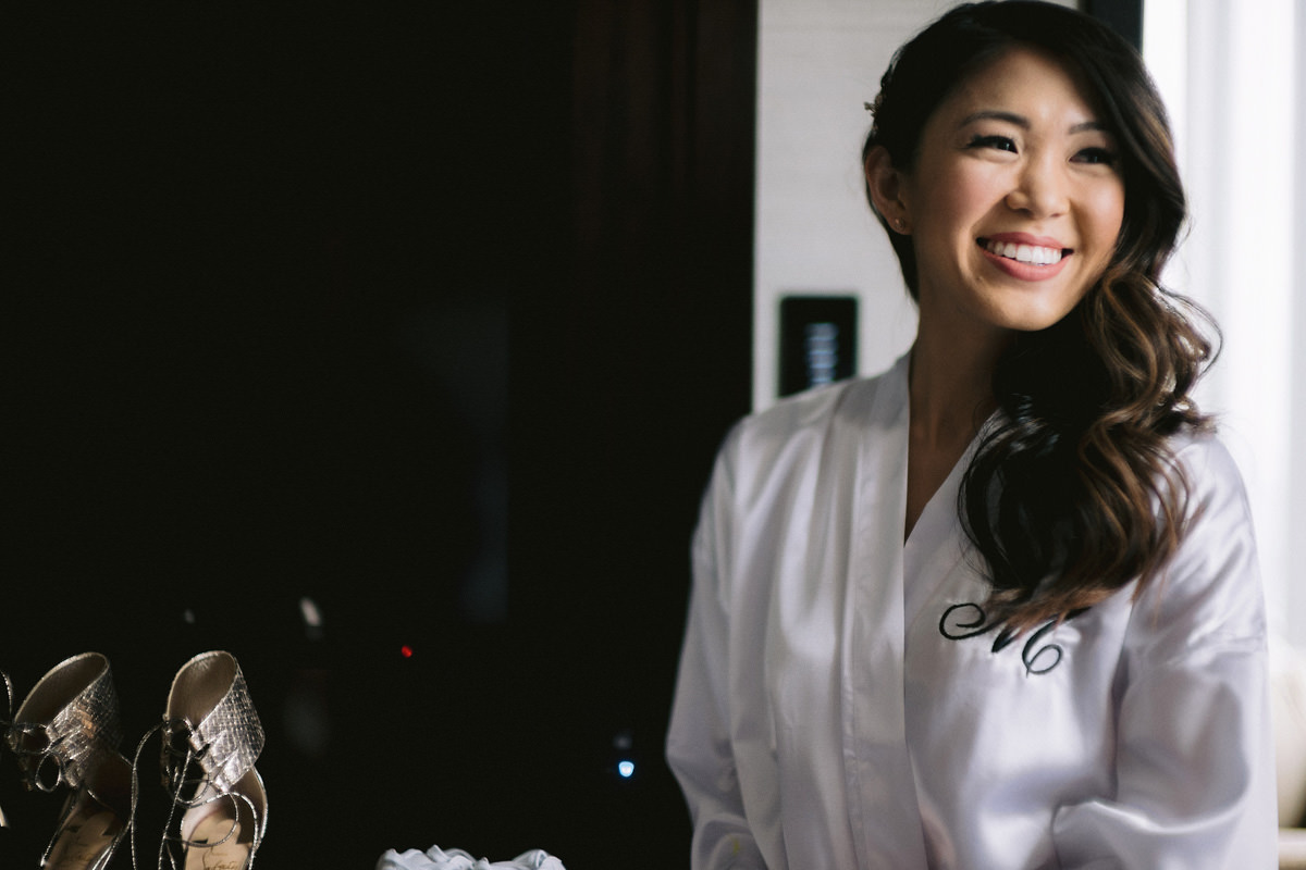 A bride smiles at the camera in her bridal robe on her wedding day