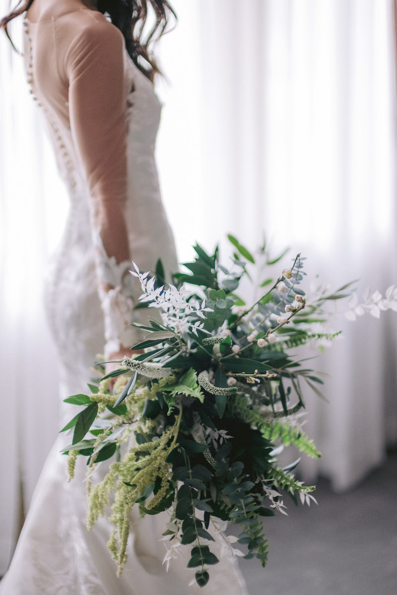 A bride holds her wedding bouquet full of greenery