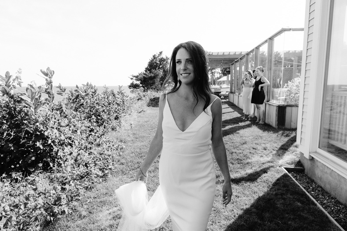 A bride holds her train while walking on the lawn at her wedding reception.