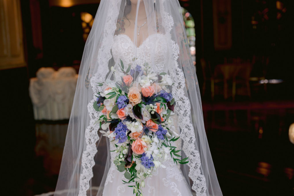 A lace trim veil and lace wedding dress with a pink and purple wedding bouquet