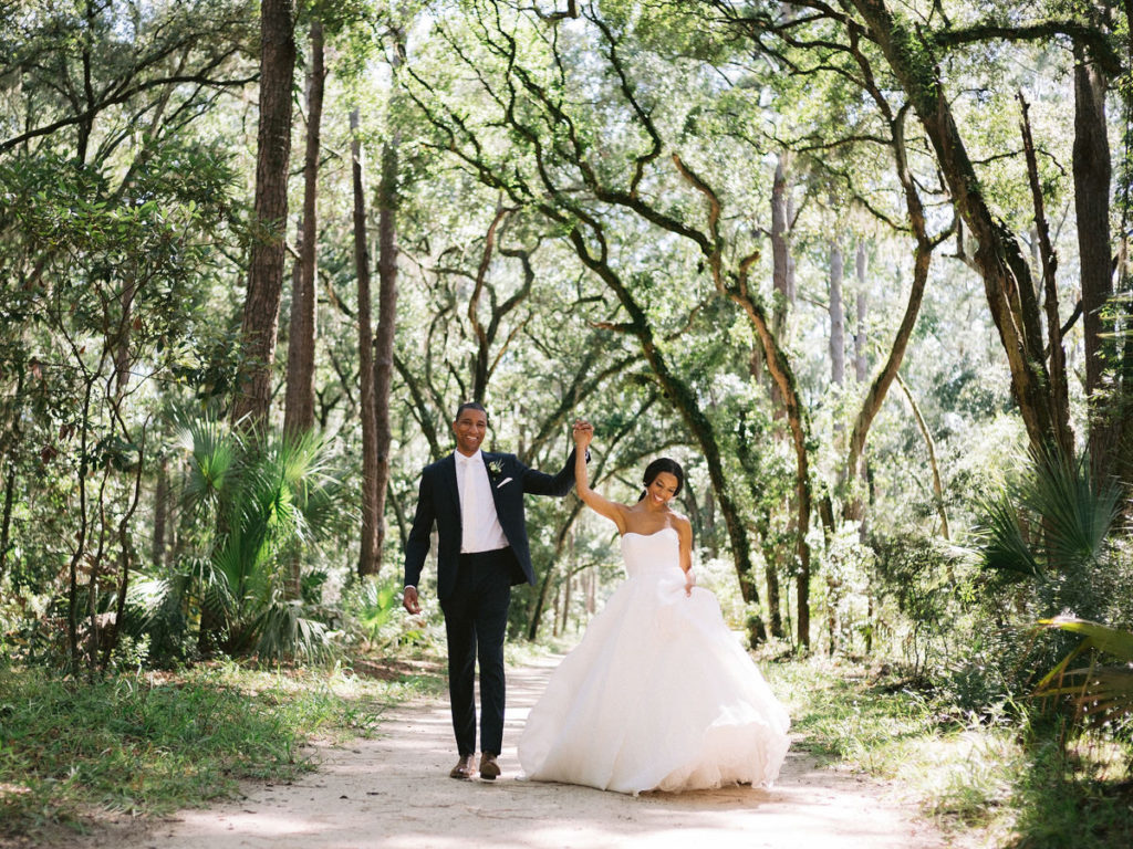 A bride in a large white dress holding hands with her groom in the forest
