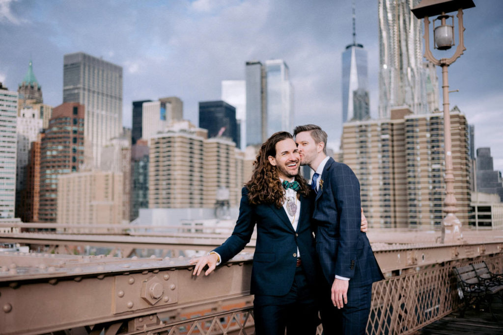 A man kisses his husband on the cheek on the Brooklyn bridge