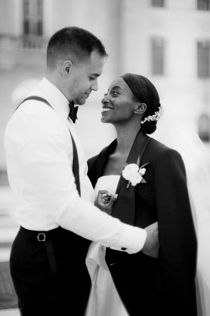 A groom looks down at his bride wearing his suit jacket