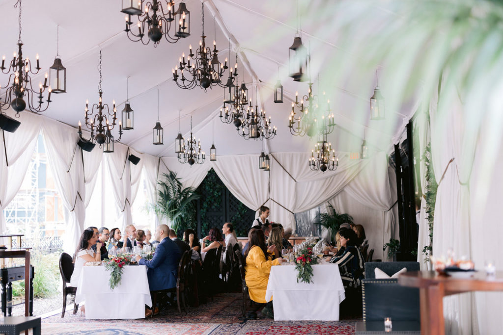 A white tent with vintage chandeliers and plants. 