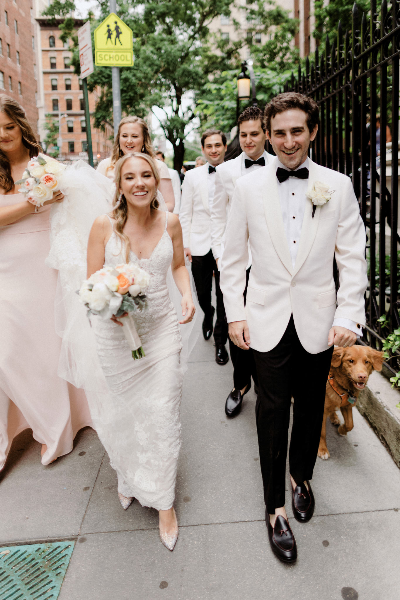 Newlyweds walk down a street with their wedding party in New York City