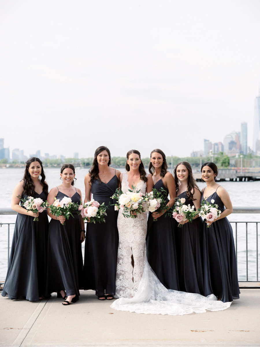 A bride and her bridesmaids smile at the camera with the New York City skyline in the background