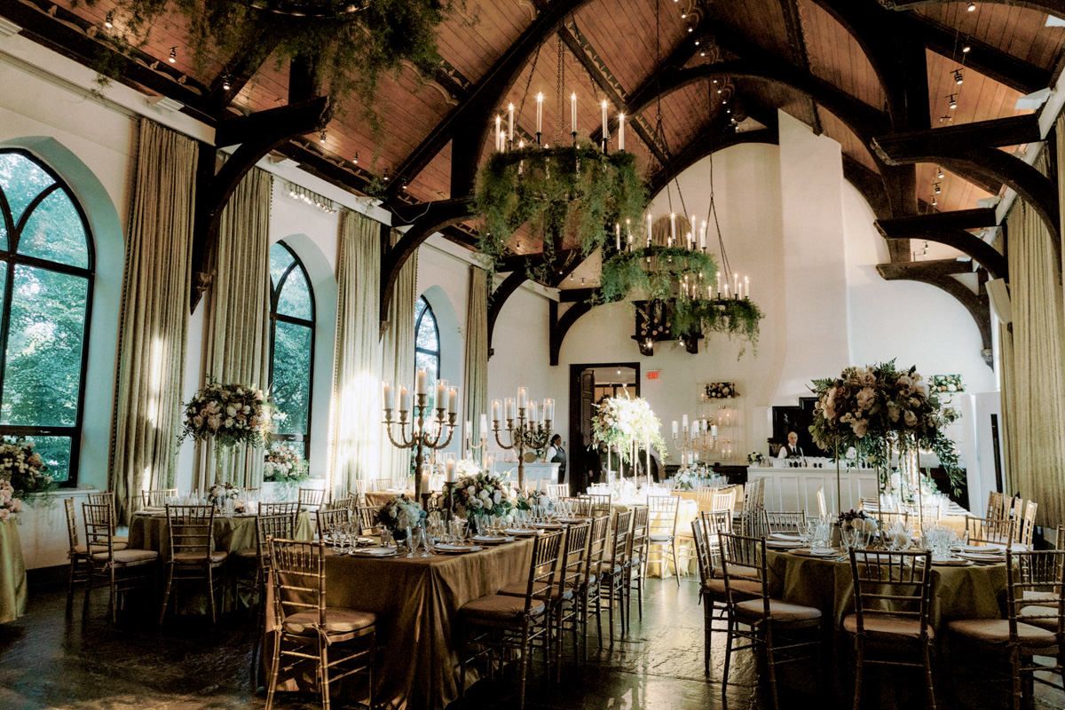 Elegant wedding venue room with chandeliers and bronze tables and chairs with large flower bouquet and candle centerpieces