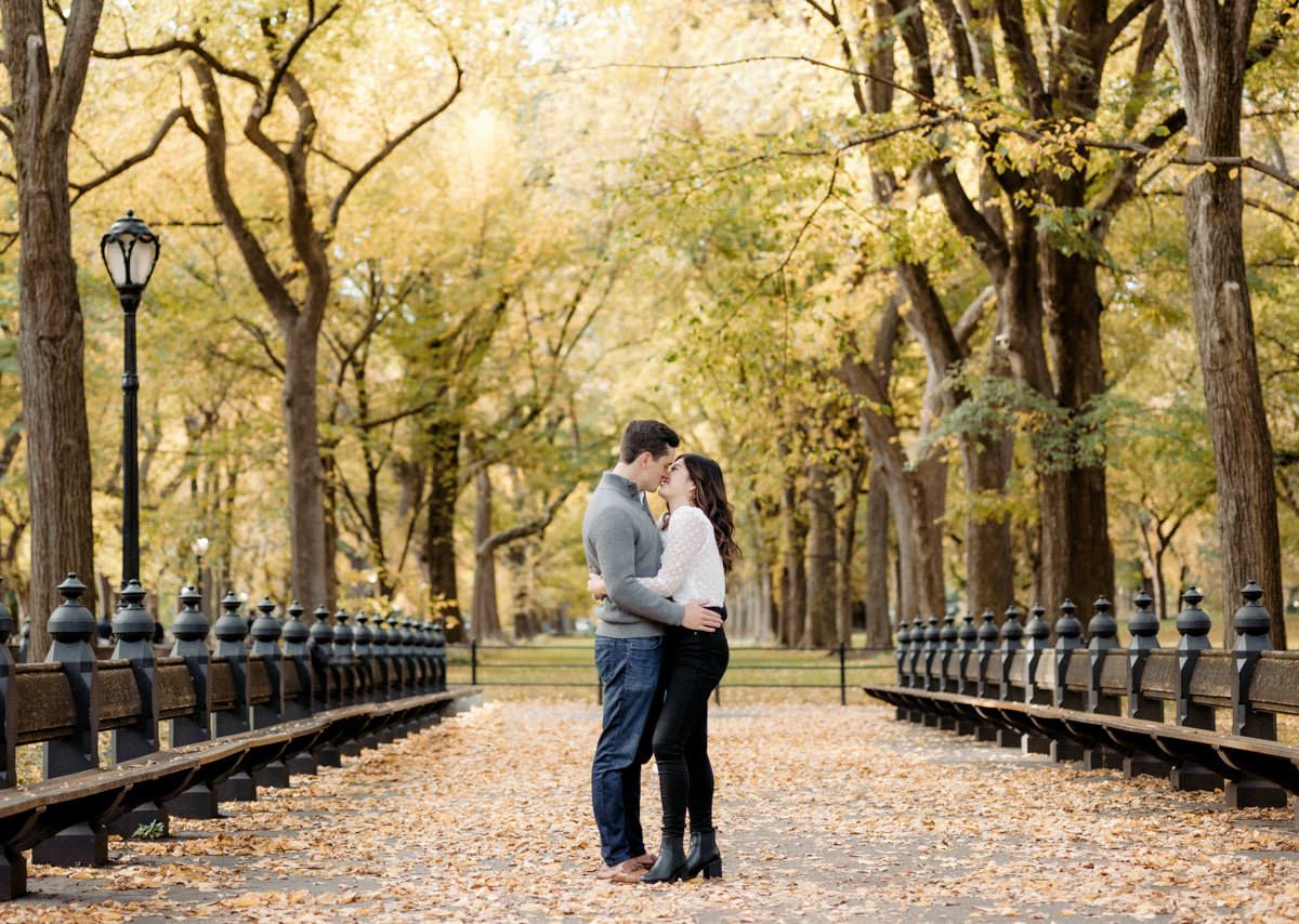 A man and woman kissing. Trees and fallen leaves on the background