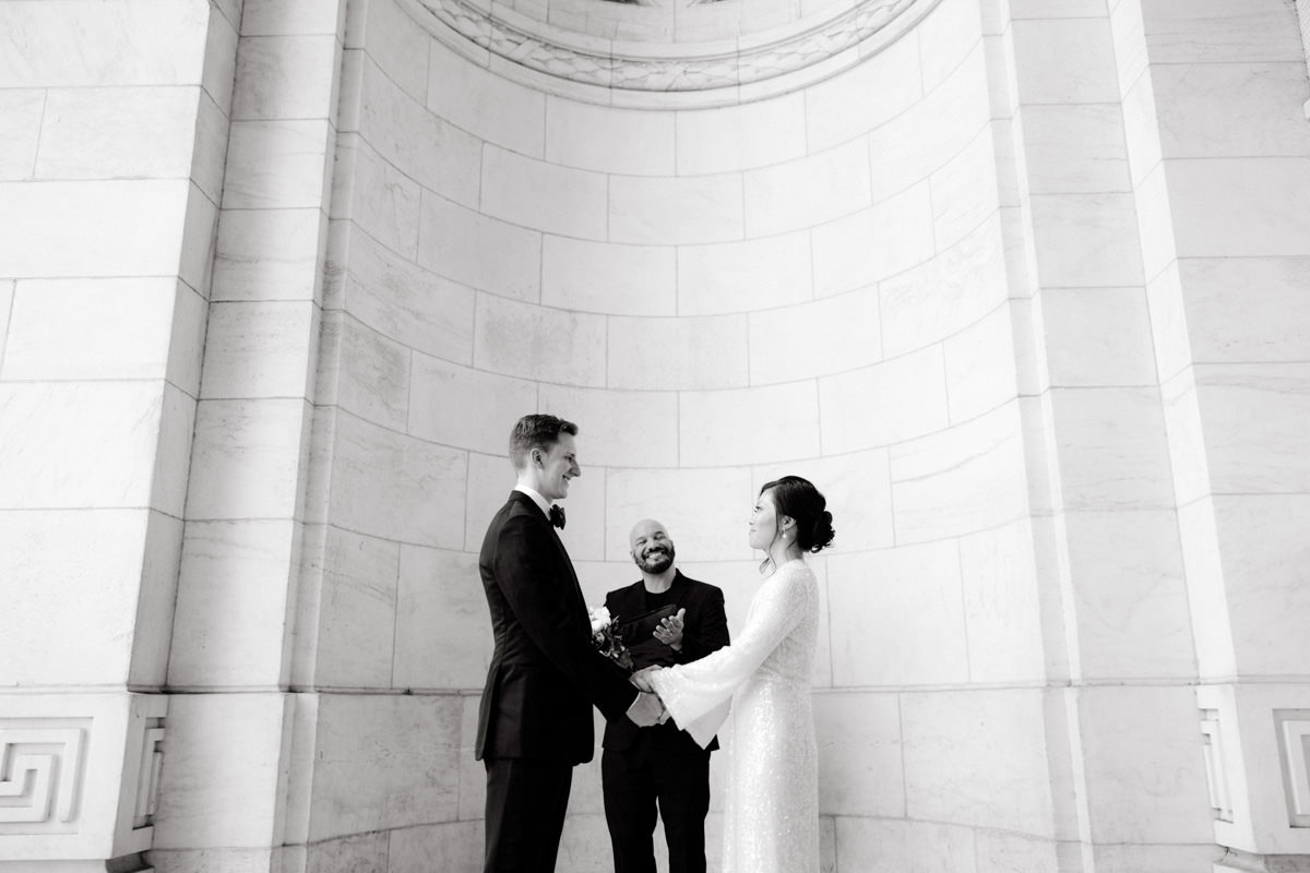 Bride and Groom holding hands, facing each other as wedding officiant smiles
