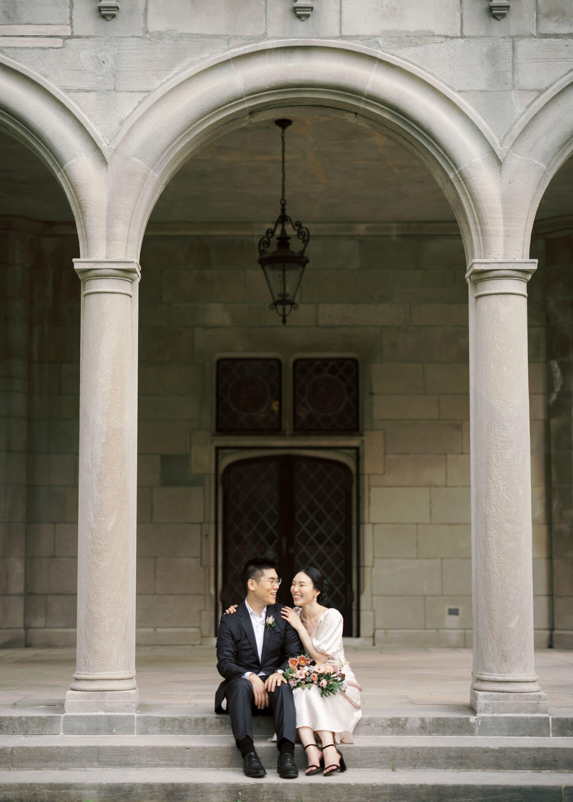 The bride and the groom are sitting on the entrance staircase in Planting Fields Arboretum, Oyster Bay, NY. Image by Jenny Fu Studio