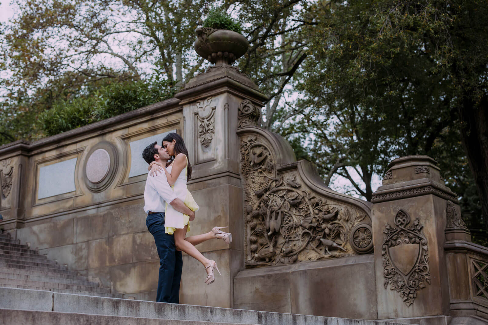 An engaged couple are kissing while the man is carrying the woman, at Central Park, NYC.