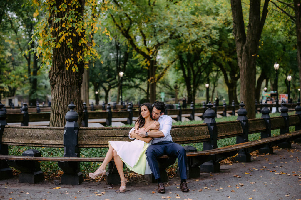 An engaged couple are romantically sitting on a bench in Central Park, NYC.