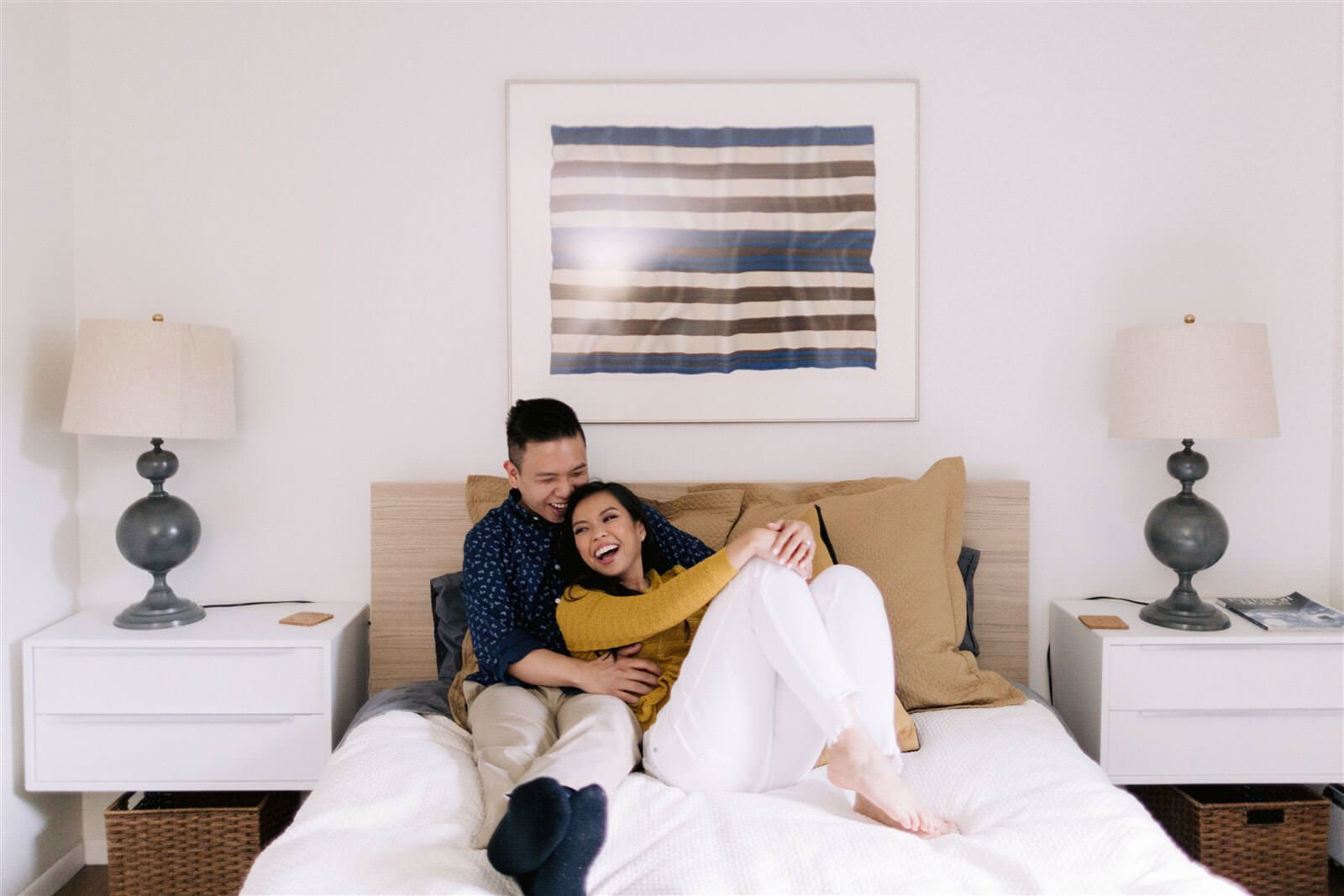 An engaged couple are laughing while sitting on a bed at Denver, Colorado
