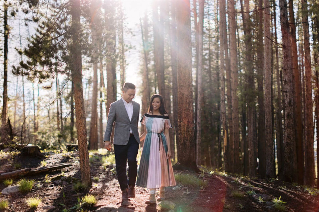 An engaged couple are walking amidst tall trees at Denver, Colorado.