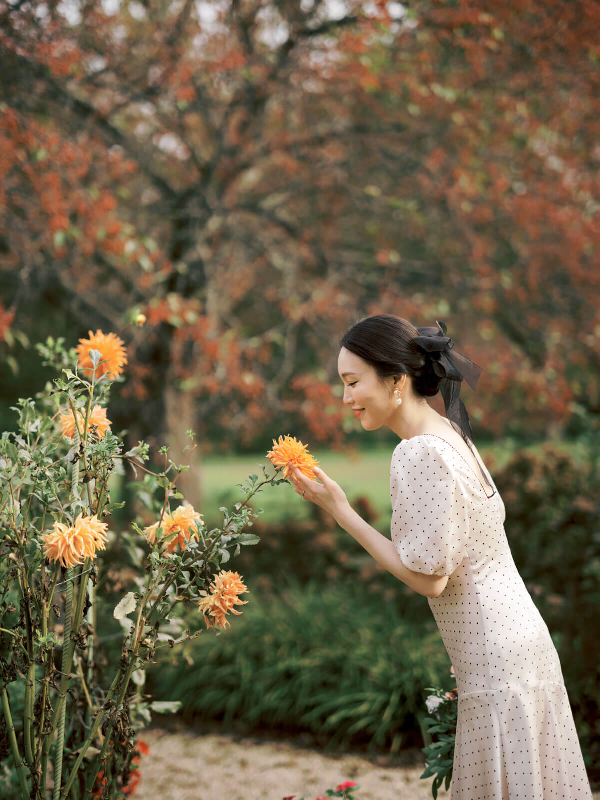 The engaged woman is happily touching a beautiful orange flower amidst the beautiful fall foliage. Image by Jenny Fu Studio