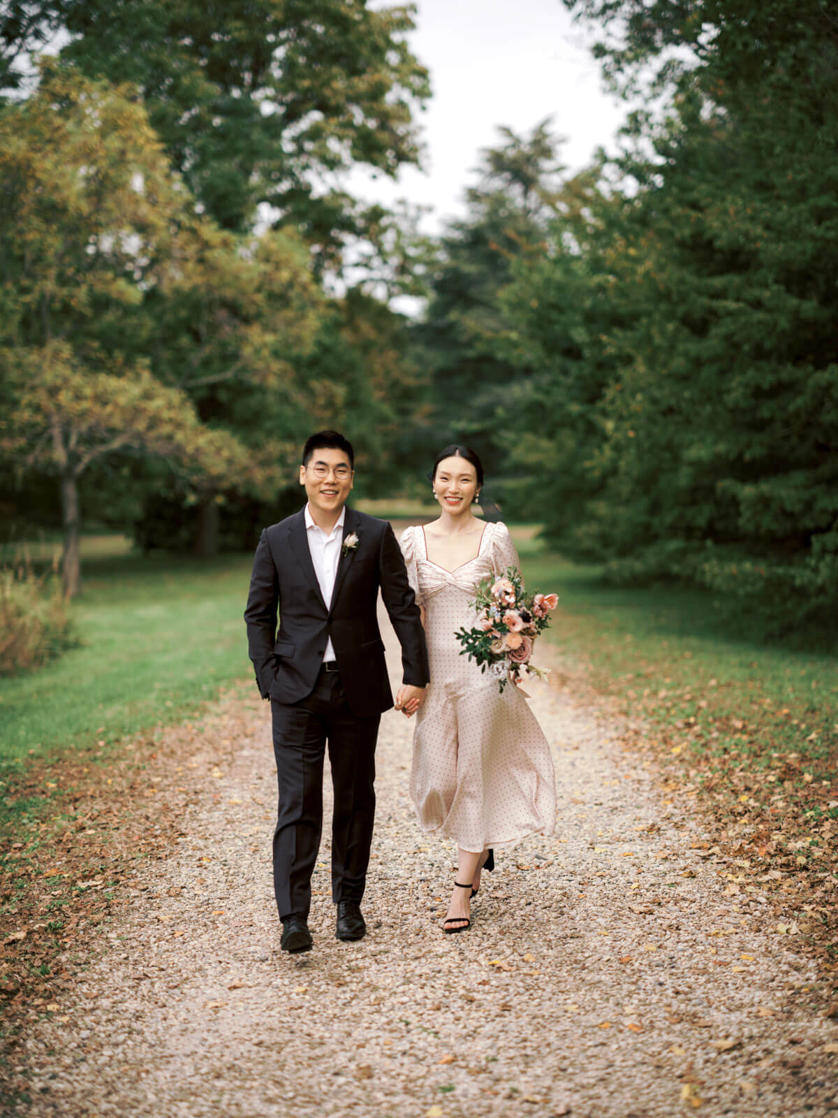 The engaged couple is standing on a trail filled with fall leaves, amidst the beautiful fall foliage. Image by Jenny Fu Studio