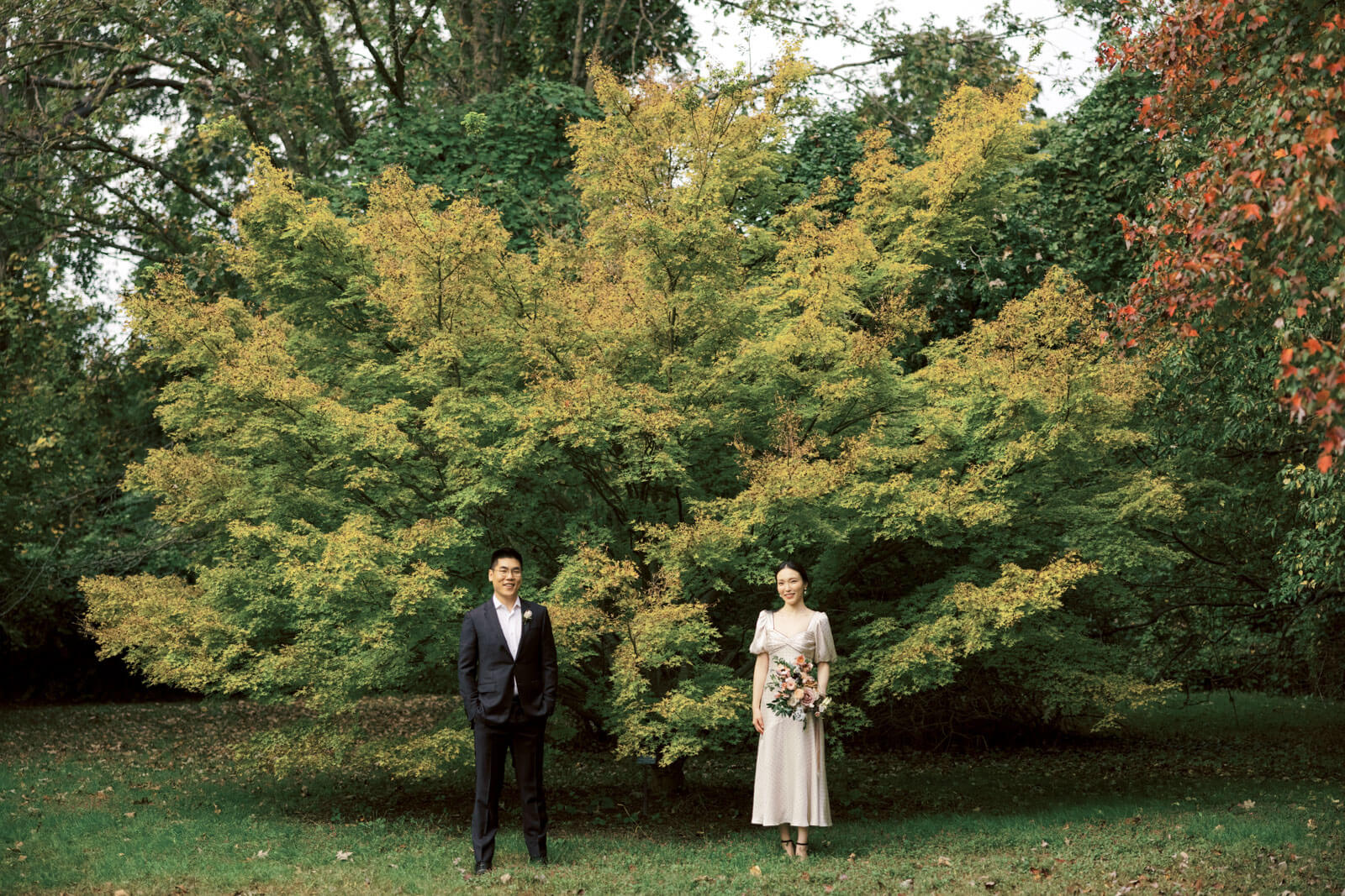 The engaged couple is standing a meter apart, amongst the beautiful fall foliage. Image by Jenny Fu Studio