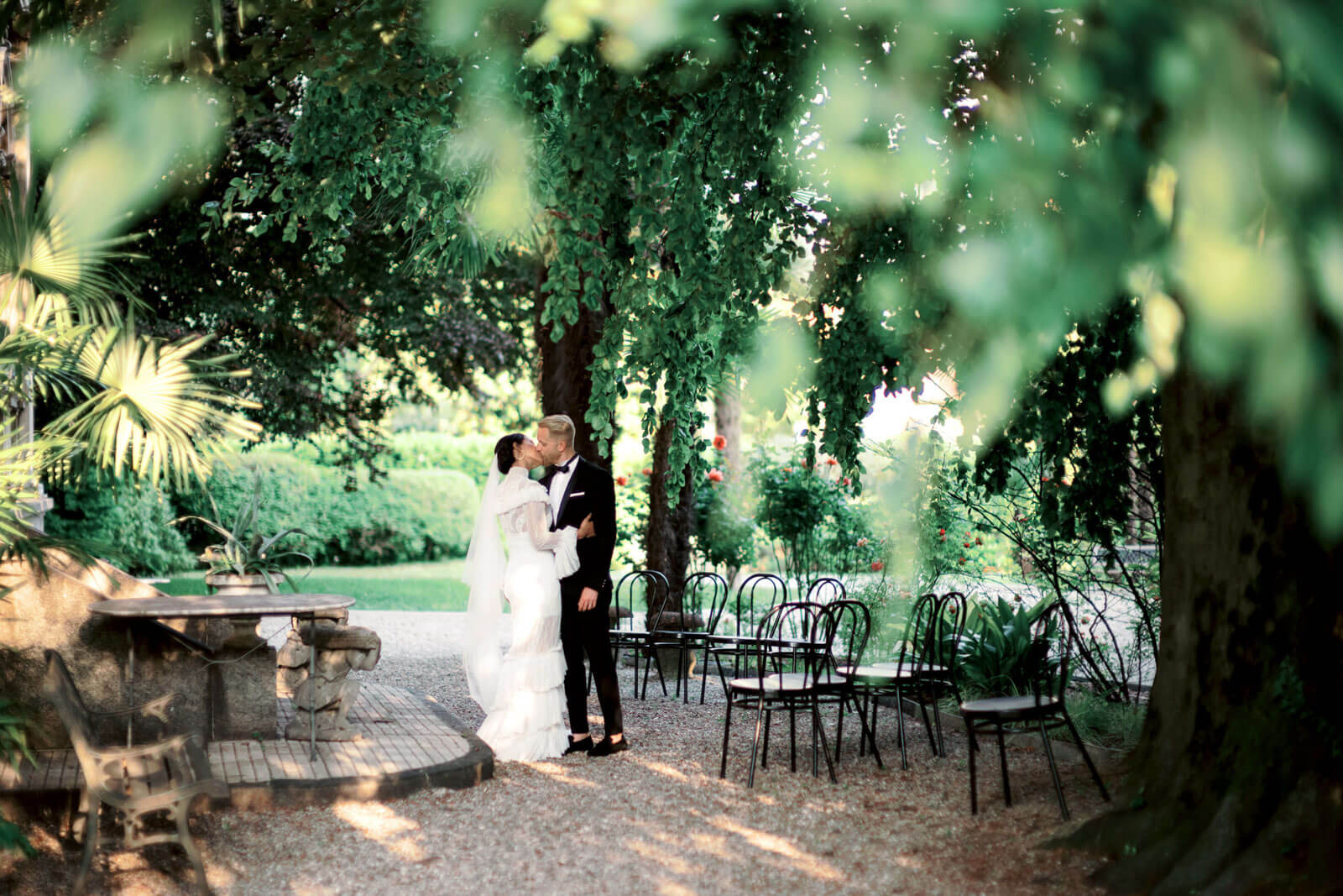bride and groom kissing underneath giant trees on wedding day in Lake Como Italy